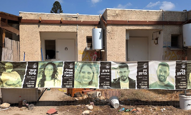 Posters calling for the return of hostages outside burned buildings in Kfar Aza