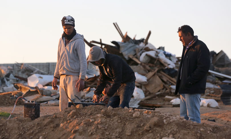 A group stands outside the remains of a demolished village